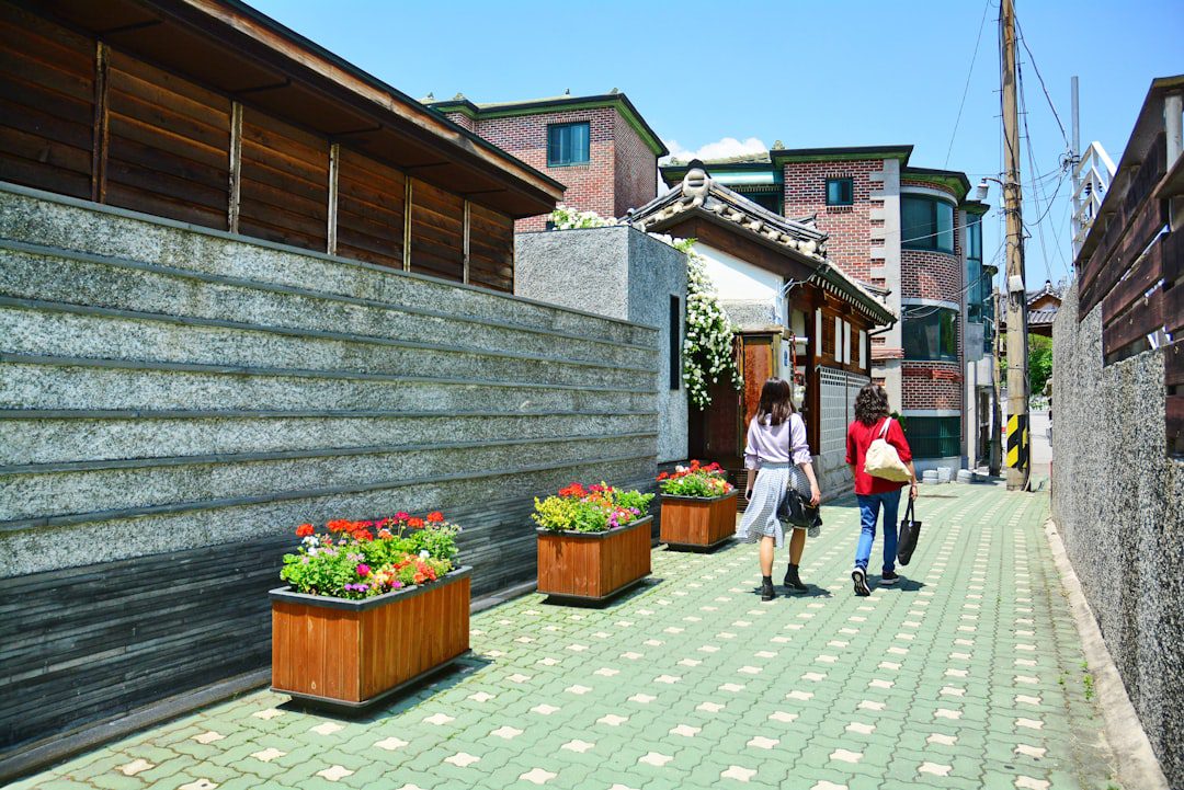 a couple of women walking down a sidewalk between stone buildings