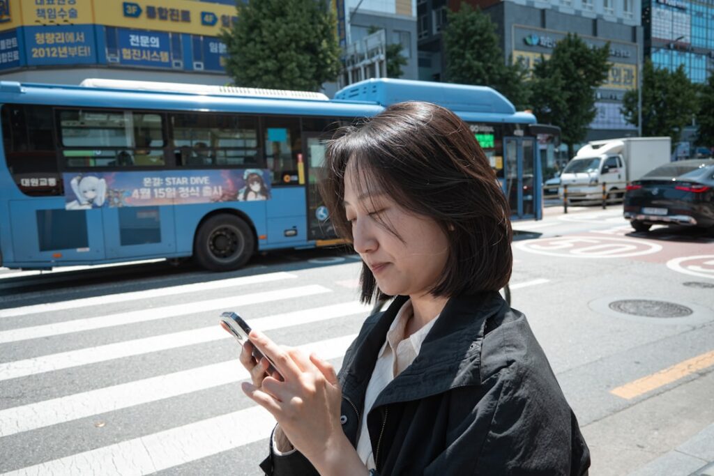 Woman looking at phone at a crosswalk with bus